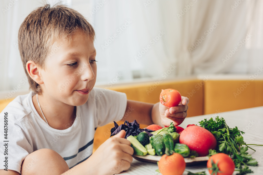 Boy sitting in the kitchen eating healthy vegetables cucumber and tomato Boy sitting in the kitchen eating healthy vegetables cucumber and tomato