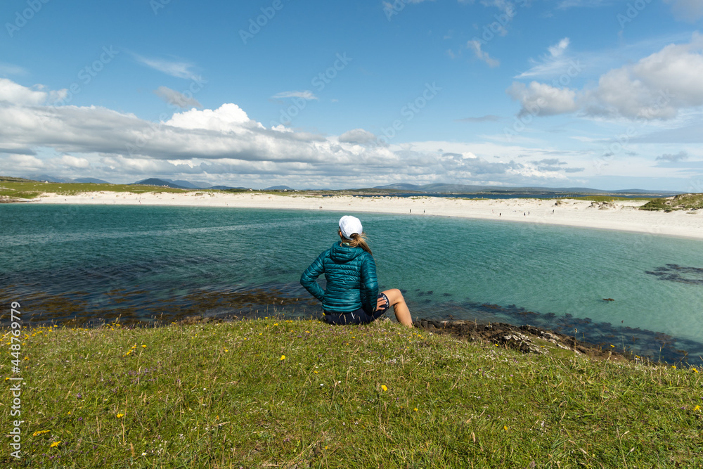 A seated woman is looking at the landscape of Dog's Bay in Galway Ireland