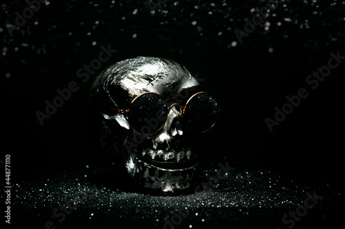 Helovin silver skull in sunglasses on black background with sparkles and boks. Concept of halloween disco party in a nightclub. Postcard mock up with space for text. photo