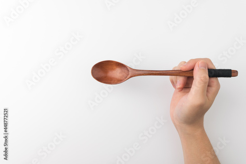 A hand holding a wooden spoon on a white background