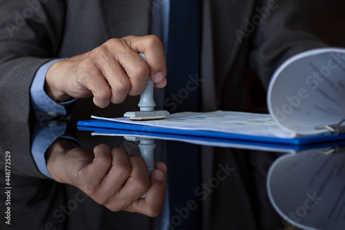 Businessman in suit hand stamping rubber stamp on document at office. Authorized allowance permission approval concept.