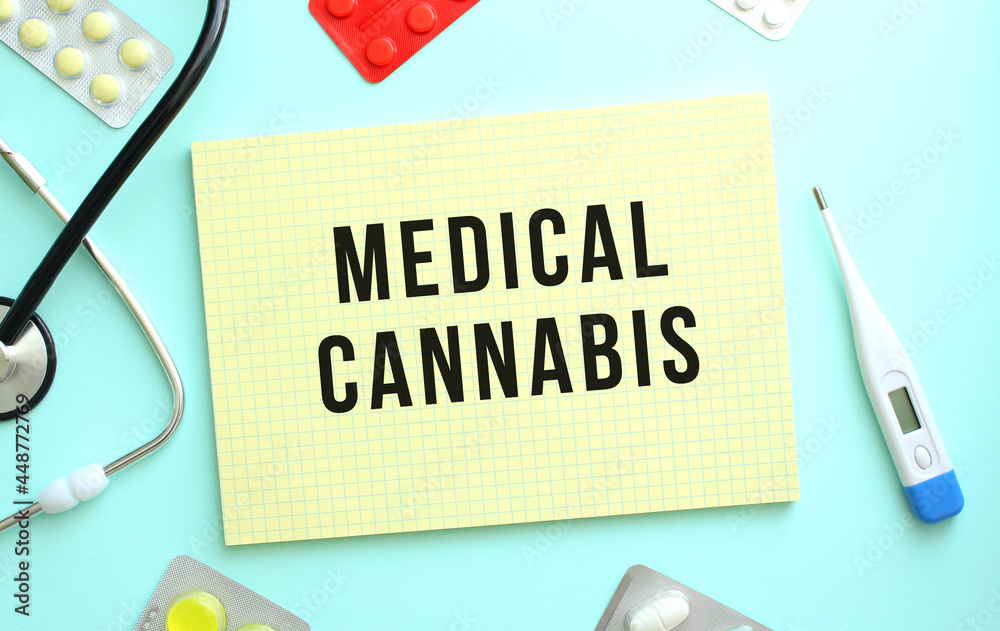 The text MEDICAL CANNABIS is written in a yellow notebook that lies next to the stethoscope on a blue background The text MEDICAL CANNABIS is written in a yellow notebook that lies next to the stethoscope on a blue background