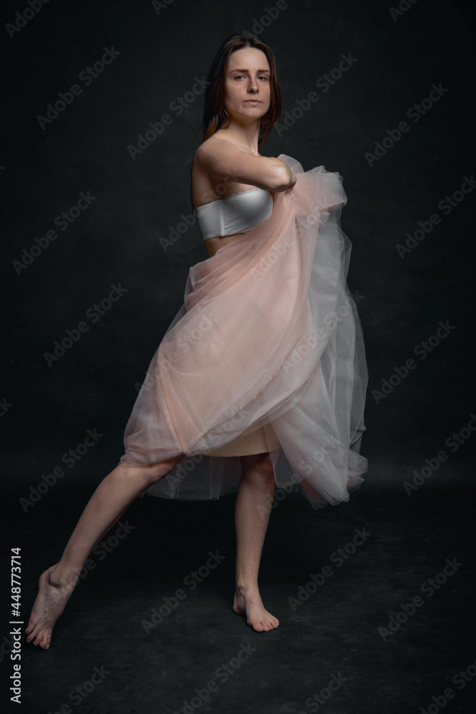 Young girl in white top and peach skirt dancing in black old textured studio