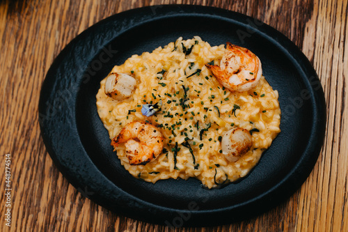 Risotto with shrimps and a flower on a black plate.