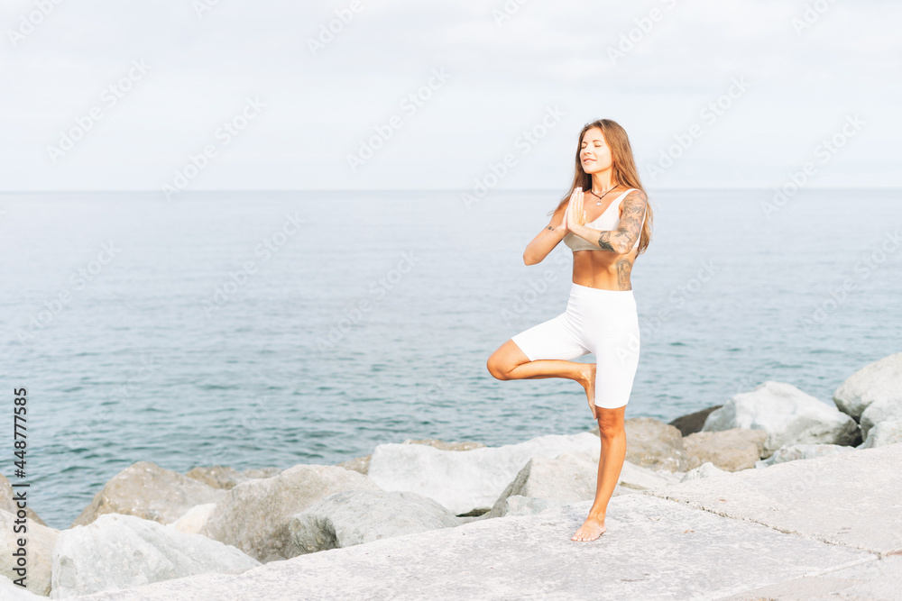 Young fit beautiful woman with long hair in white sport clothes practice yoga and enjoy life on the sea beach, mental and phisical health Young fit beautiful woman with long hair in white sport clothes practice yoga and enjoy life on the sea beach, mental and phisical health