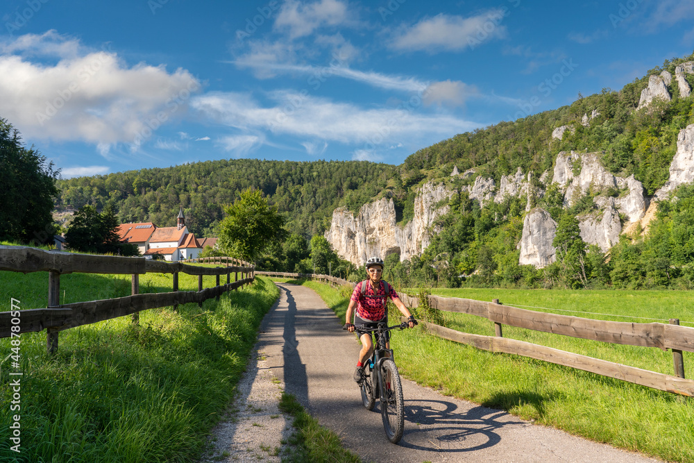 beautiful active senior woman cycling with her electric mountain bike in the rocky Upper Danube Valley on the Swabian Alb between Beuron and Sigmaringen