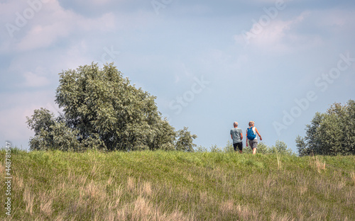 Unidentified man and woman walking on top of a Dutch dike on a sunny day in the summer season. © Ruud Morijn
