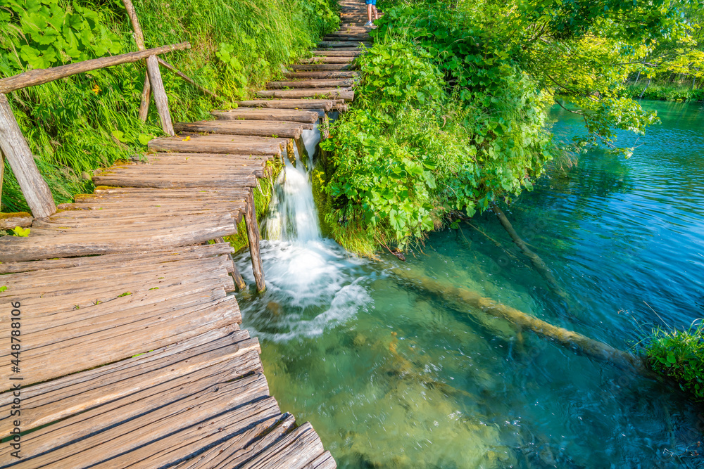 Obraz premium Wooden footpath at Plitvice national park, Croatia. Pathway in the forest near the lake and waterfall. Fresh beautiful nature, peaceful place. Famous tourist destination.