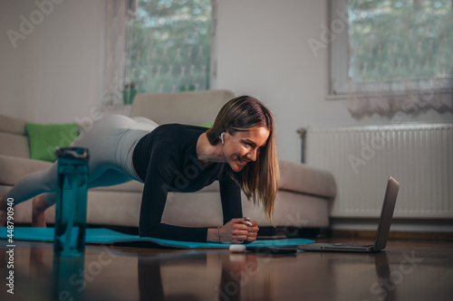 Woman in a plank position while using laptop for her online fitness training at home
