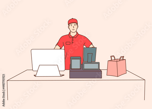 Young male employee cashier, worker using modern technology at workspace. Young smiling man cash register at the workplace in supermarket, shop.