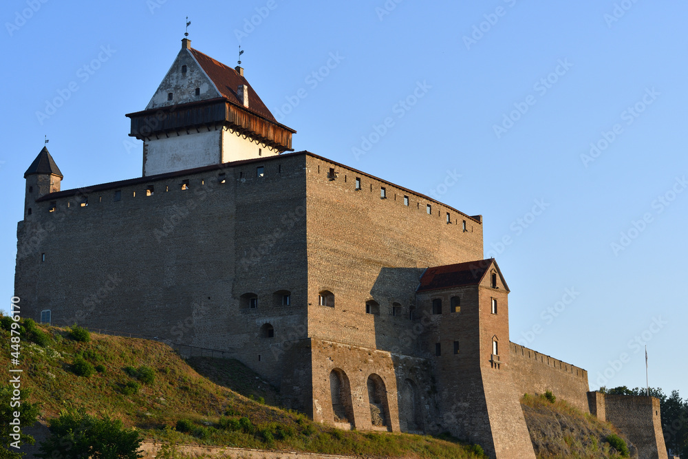 Narva Castle, Estonia, under a clear blue sky in the yellow direct sunlight of sunrise, a combination of harsh cold shadows and rich warm light, a sky from bright blue to pale below.
