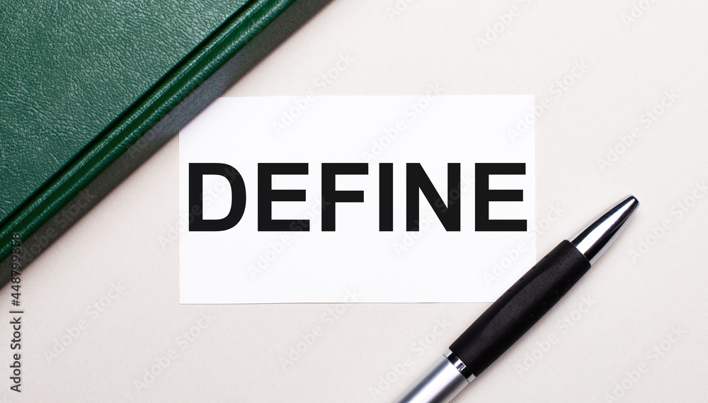 On a light gray background lies a pen, a green notebook and a white card with the text DEFINE. Business concept. On a light gray background lies a pen, a green notebook and a white card with the text DEFINE. Business concept.