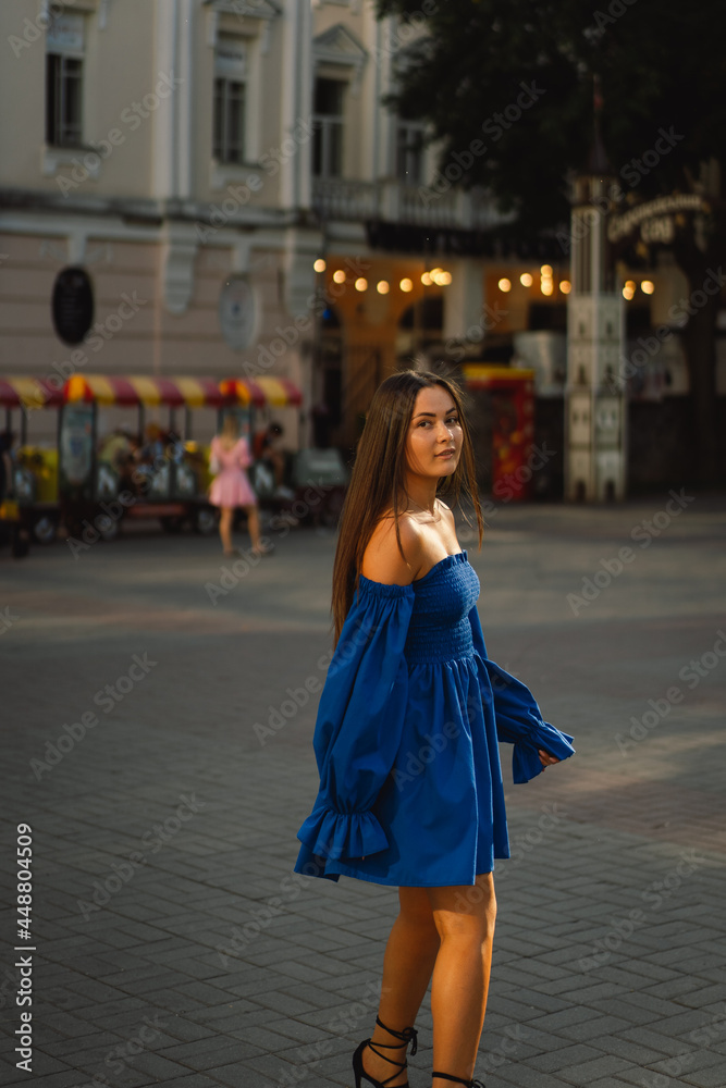 Portrait happy young woman wearing blue dress laughing looking at camera standing on street. Urban background
