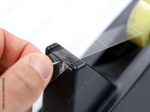 male hand is using a black dispenser of a transparent tape isolated on white background, close up photo