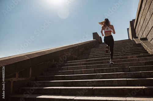 Sportive lady in tracksuit runs up old stone steps under clear sky