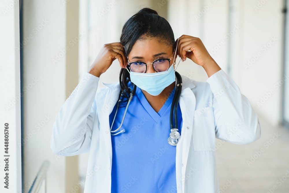 Portrait of african american female doctor wearing mask standing in hospital corridor. medicine, health and healthcare services during coronavirus covid 19 pandemic. Portrait of african american female doctor wearing mask standing in hospital corridor. medicine, health and healthcare services during coronavirus covid 19 pandemic.