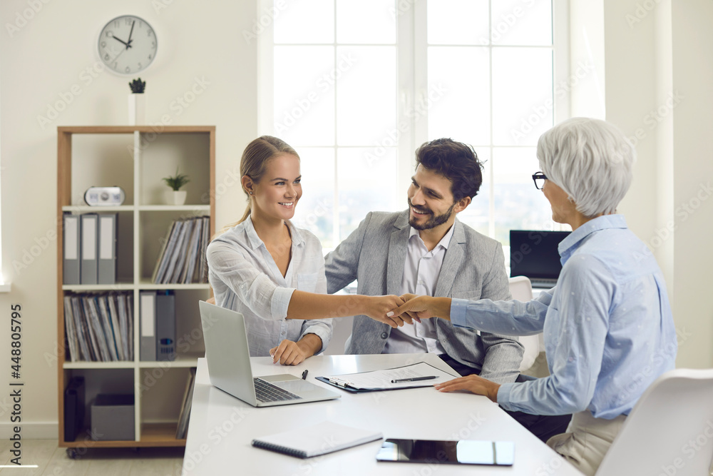 Happy clients shaking hands with bank manager. Married couple sitting at office desk exchanging handshake with mortgage advisor. Future house buyers thanking real estate agent for consultation meeting Happy clients shaking hands with bank manager. Married couple sitting at office desk exchanging handshake with mortgage advisor. Future house buyers thanking real estate agent for consultation meeting