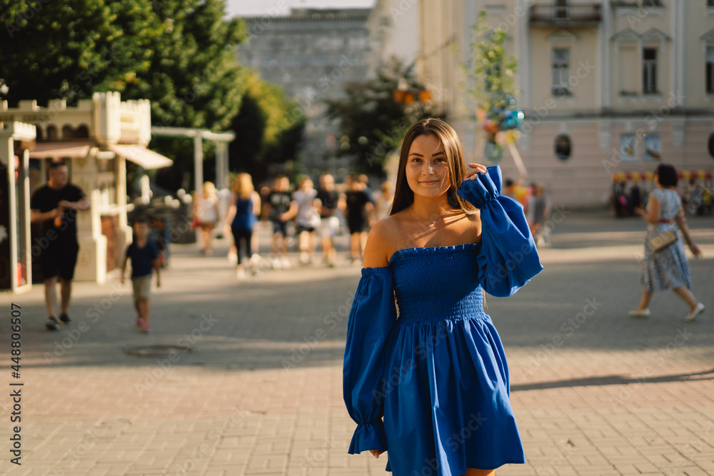 Fototapeta premium Portrait happy young woman wearing blue dress laughing looking at camera standing on street. Urban background