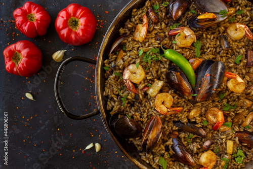Vászonkép Close up of a traditional spanish black paella with shrimps, mussels and squid ink in a pan with tomatoes on a black background