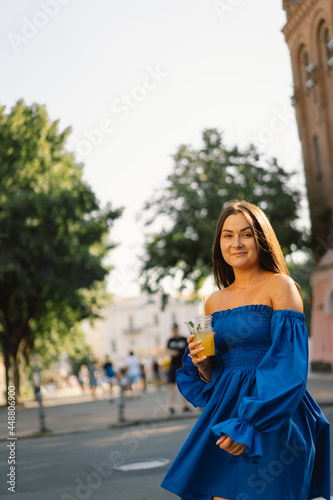 Portrait happy young woman wearing blue dress and drinking summer cocktail lemonade