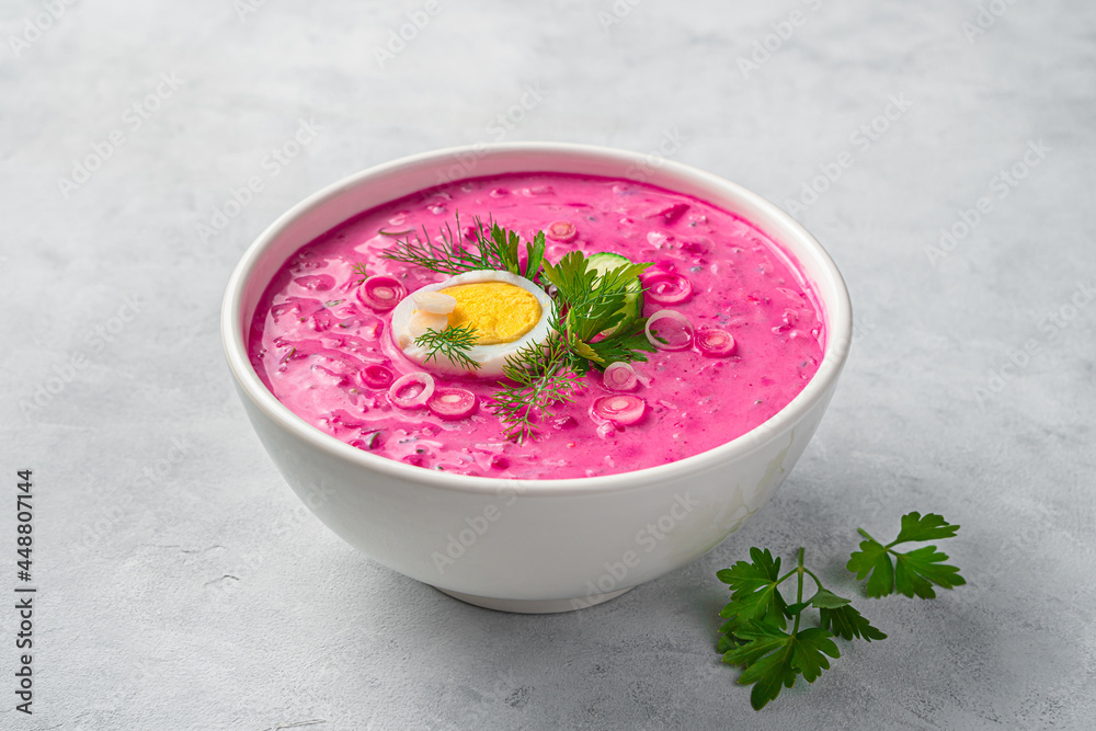 A plate of cold beetroot soup with egg and herbs on a gray background. Side view, close-up. Healthy, vegetarian food. A plate of cold beetroot soup with egg and herbs on a gray background. Side view, close-up. Healthy, vegetarian food.