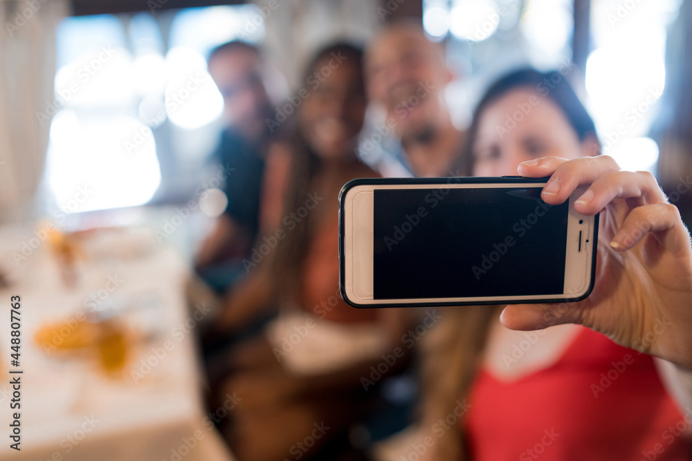Group of friends taking a selfie with a mobile phone at a restaurant.