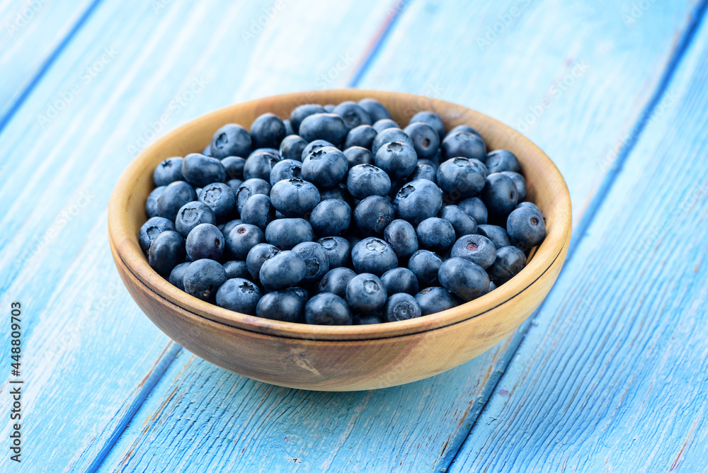 Fresh blueberries in a wooden bowl on an old blue wooden table. Healthy and dietary food concept. Blueberry is an antioxidant