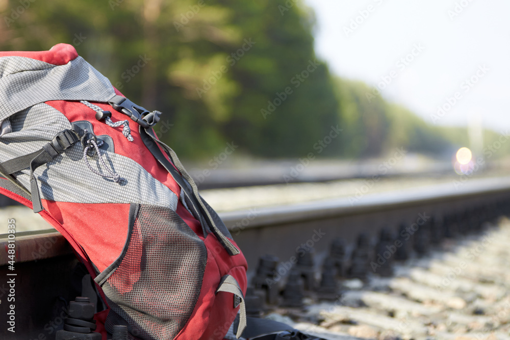 Red backpack at the railway on the background of a pine forest and the lights of the approaching train. Travel concept