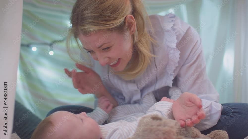 Loving mother playing peek-a-boo with baby son lying on rug in homemade camp in child's bedroom at home - shot in slow motion Loving mother playing peek-a-boo with baby son lying on rug in homemade camp in child's bedroom at home - shot in slow motion
