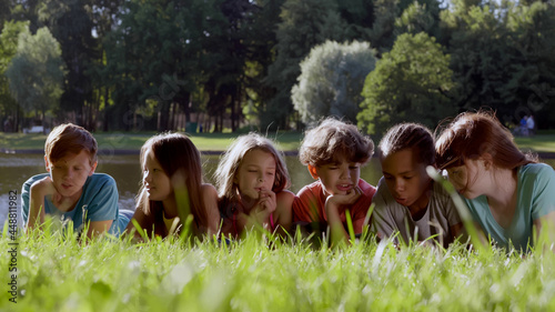 Joyful multiracial preteen friends lying on park grass together