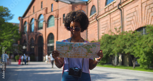 Cheerful afro woman wanderer searching direction on location map traveling abroad in summer photo