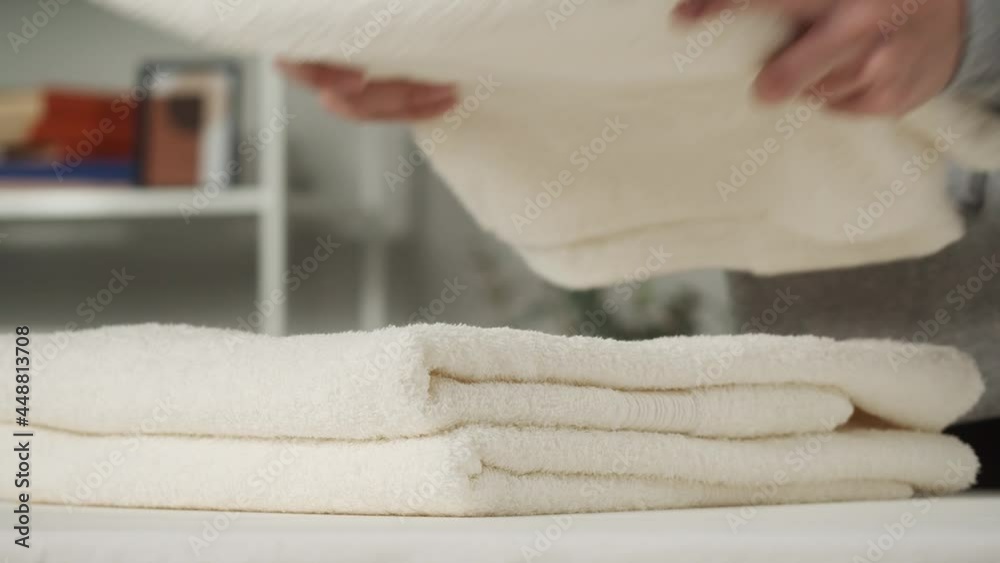 Young woman putting washed dry clean towels on iron board, preparing for ironing. Housewife doing household chores. Cleaning service in hotels. Laundry room with professional electric equipment. Young woman putting washed dry clean towels on iron board, preparing for ironing. Housewife doing household chores. Cleaning service in hotels. Laundry room with professional electric equipment.