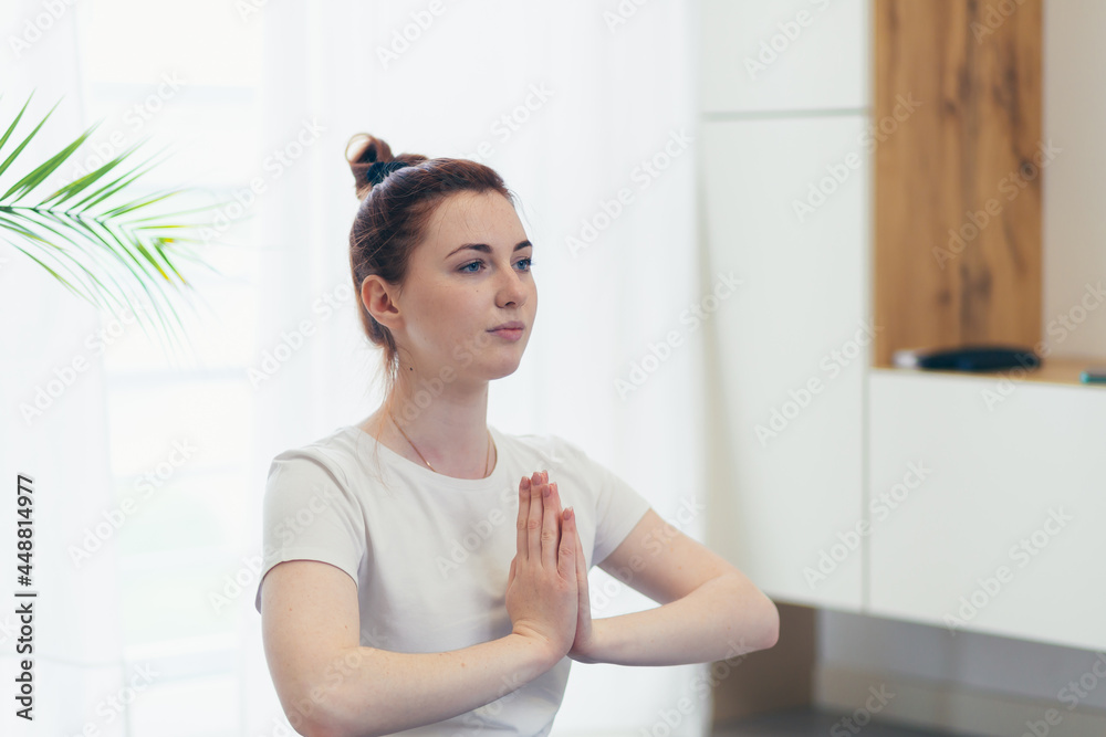 young attractive woman is practicing yoga online using a mobile phone or smartphone app. Female yogi morning in casual clothes at home in living room, workout lotus position meditates on a mat young attractive woman is practicing yoga online using a mobile phone or smartphone app. Female yogi morning in casual clothes at home in living room, workout lotus position meditates on a mat