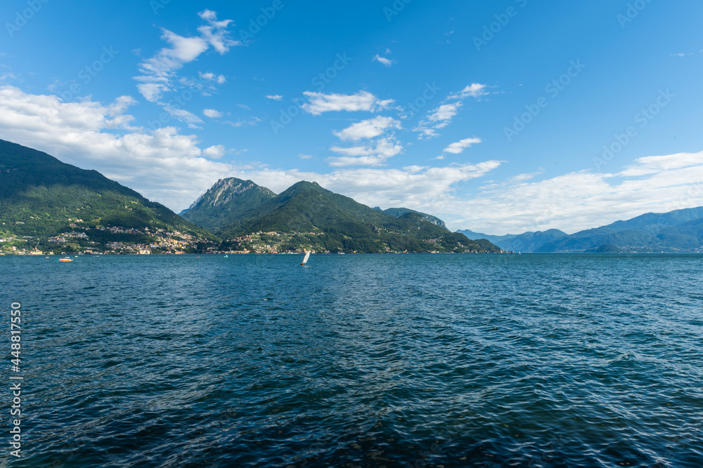 View over the beautiful, gorgeous lake Como seen from the small village of Santa Maria Rezzonico. It is a beautiful sunny summer day, with blue sky and a few clouds. There are boats on the lake.