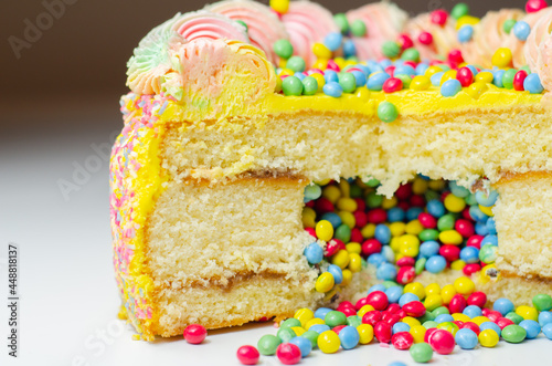 Madeira sponge coated with yellow colour frosting, layered with plum and raspberry jam, filled and topped with multicolour chocolate nibs and decorated with multicolour frostings and sugar decorations