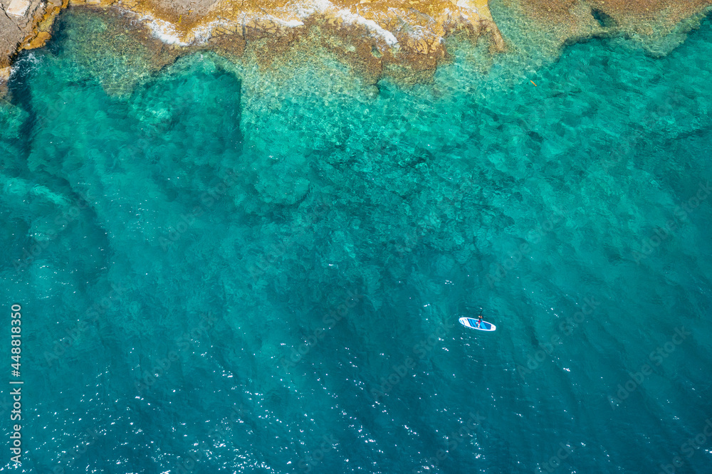 Top view on the man on the stand up paddleboard SUP in the sea with clear turquoise water with rocks at depth