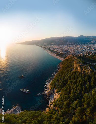 Vertical photo. Wide aerial view from Kalesi Castle peninsula. Alanya, southern coast of Turkey, Summer sunset. Travel and vacation. Ships and boats in the mediterranean. Cleopatra beach and lake