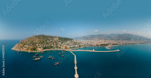 Fototapeta Naklejka Na Ścianę i Meble -  Aerial wide panoramic view of Alanya in southern coast of Turkey, Summer morning day. Travel and vacation. Kalesi Castle. Ships and boats in the mediterranean. Kızılkule bay. lighthouse and pier