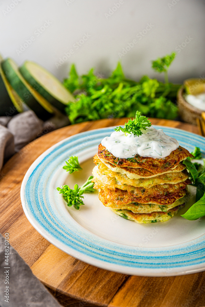 Zucchini pancakes with herbs and sour cream on a blue plate close-up vertical photo. Vegetarian dish