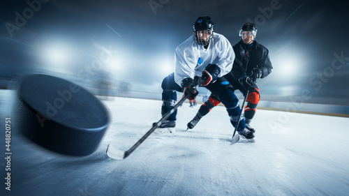 Blurred Motion Shot with 3D Flying Puck. Two Professional Ice Hockey Players on Arena From Different Teams Fighting for the Puck with Sticks. Athletes Play Intense Game Wide of Energy Competition