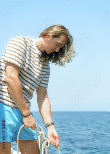 Young attractive man on a yacht making a knot photo