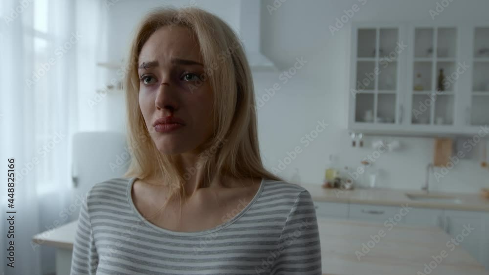 Young stressed woman with beaten face crying, standing alone at kitchen interior, need help and support, empty space Young stressed woman with beaten face crying, standing alone at kitchen interior, need help and support, empty space