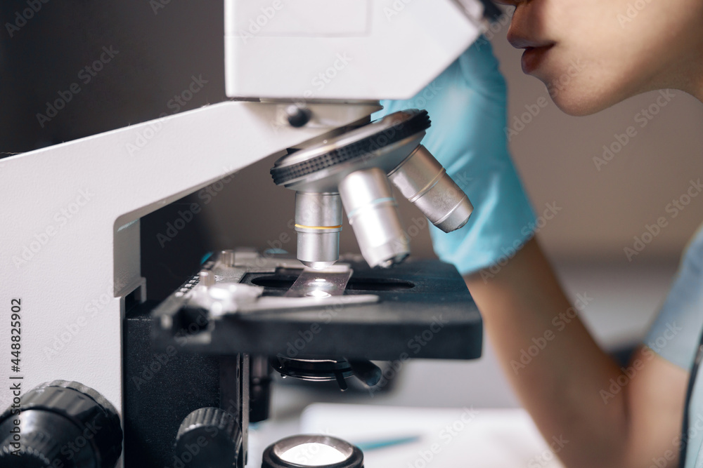 Employee in gloves looks at sample through microscope at workplace in laboratory Employee in gloves looks at sample through microscope at workplace in laboratory