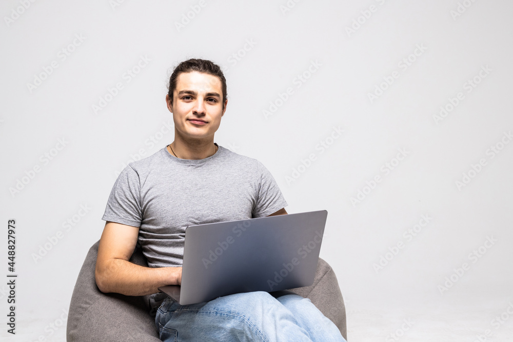 Nice photo of handsome young man using laptop and sitting on big cushioned frameless chair isolated on white background. Nice photo of handsome young man using laptop and sitting on big cushioned frameless chair isolated on white background.