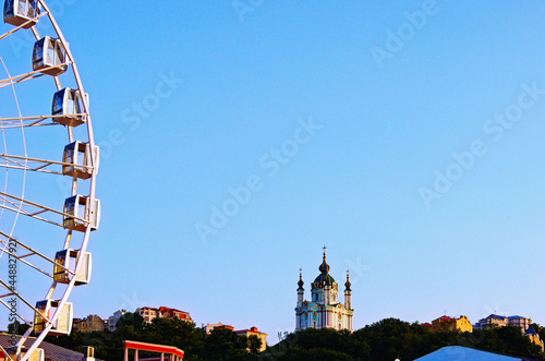 Scenic landscape view of blue sky during summer sunset in Kyiv. Part of ferris wheel on Kontraktova Square and ancient Saint Andrew s Church in the top of the hill. Abstract landscape