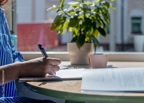 Canvas Print Student hands close up writing with pen in notepad, taking notes, studying with textbook in modern cafe with coffee cup and plant