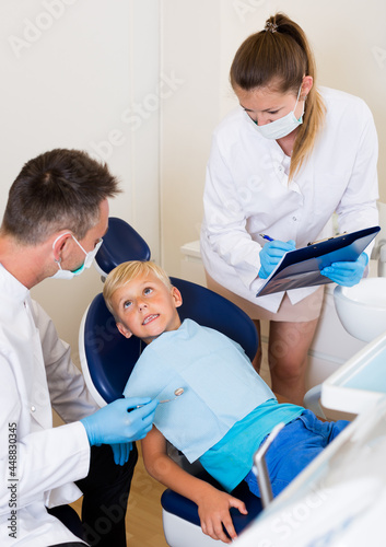 Dentist guy with assistant are diagnosticating to young patient which is sitting in dental clinic.