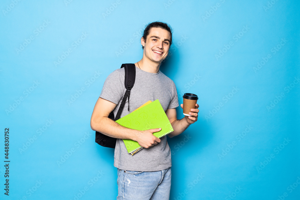 Young handsome man with backpack, headphones and cup of coffee on blue background Young handsome man with backpack, headphones and cup of coffee on blue background