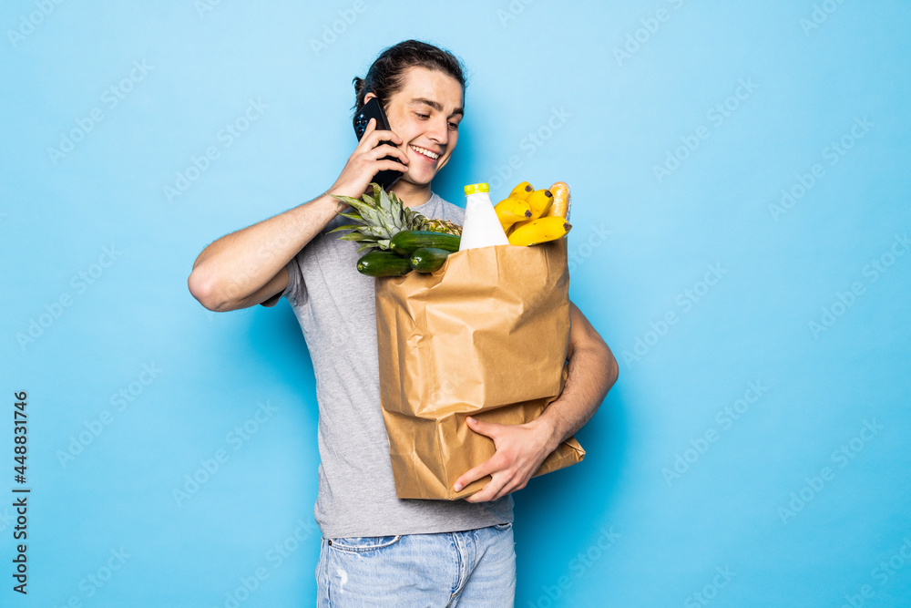 Young handsome man with his grocery shopping on blue background Young handsome man with his grocery shopping on blue background