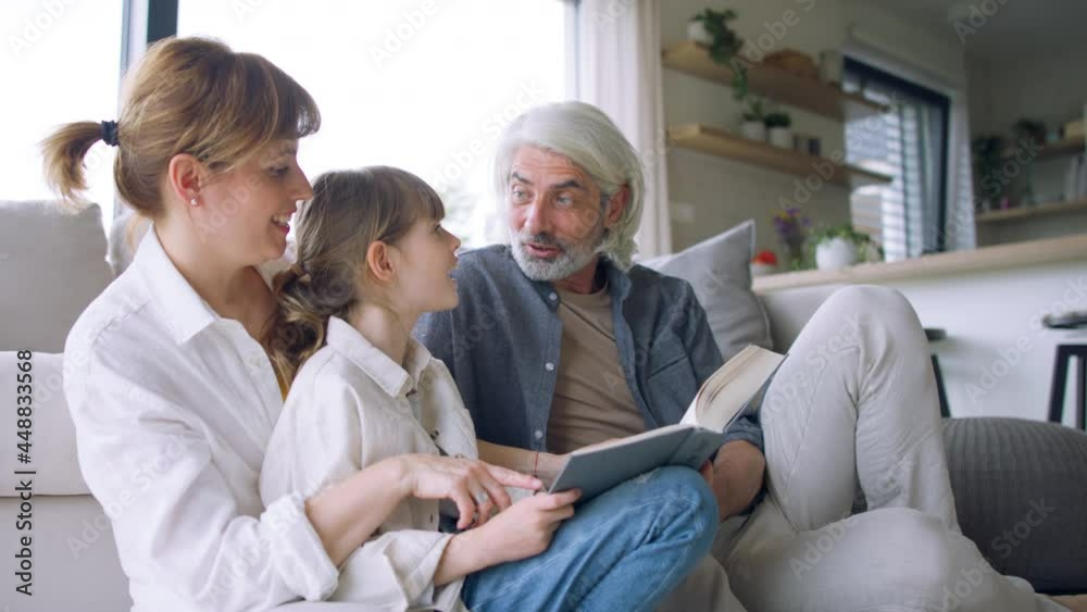 Beautiful family at home, sitting on sofa and reading a book together.